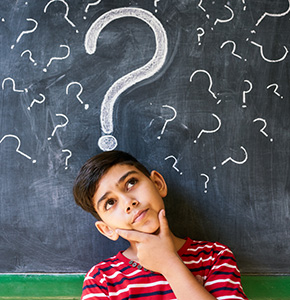 Boy thinking with various sized question marks on a chalkboard behind him